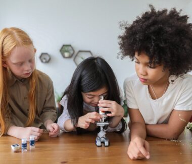 A group of three children conducting a lab experiment with a microscope.